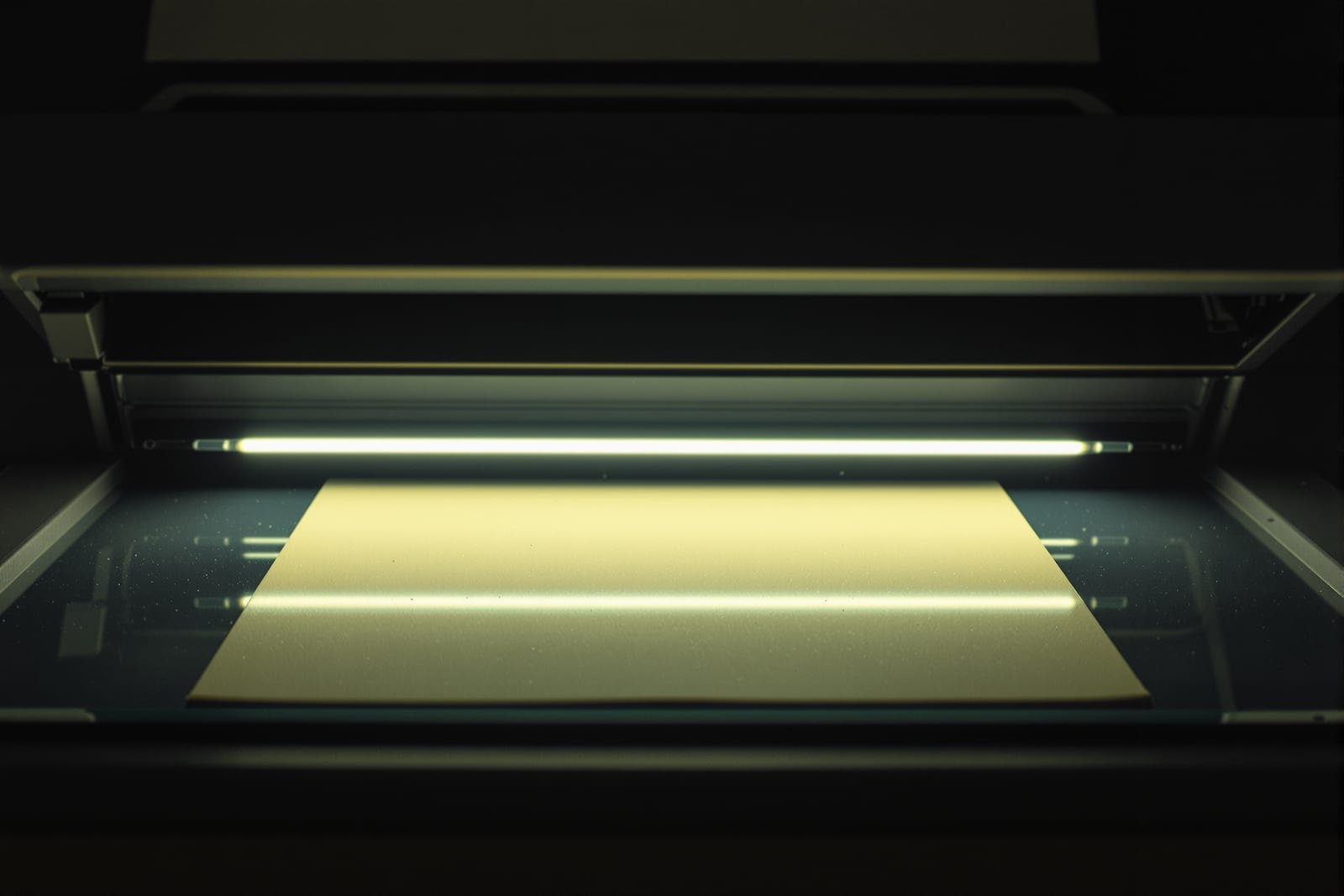 A flatbed scanner mid-sweep, its lamp bar lit beneath the glass platen with a blank sheet in place